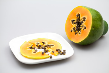 Papaya fruit - half and slice with seeds and light grey background
