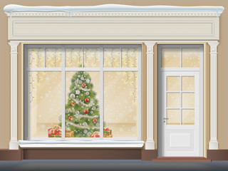 The storefront is with a door and a large window. Christmas showcase decorated with a xmas tree, glowing garland, snowflakes and gift boxes.