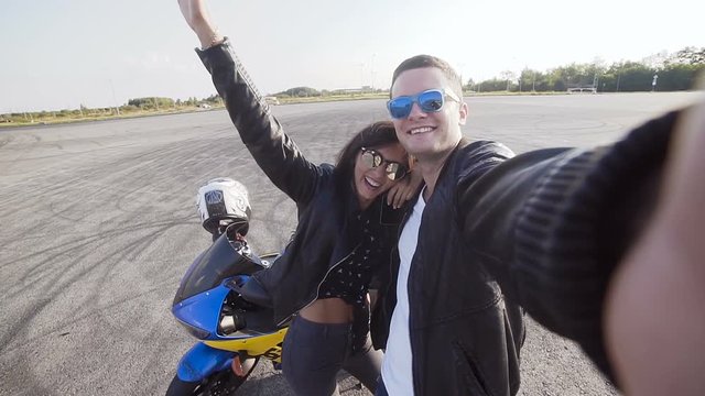 Two friends motorcyclists young guy and young girl wearing sunglasses do sephi at sunset near a motorcycle