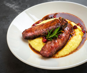 grilled sausages with mashed potatoes in a white plate on a stone background