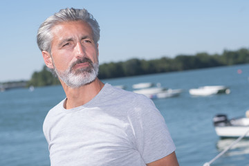 handsome man posing in front of sailing boats and lake