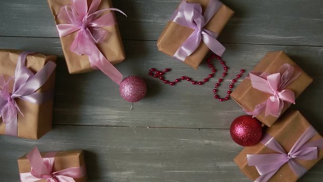 A top-down plan. Fully visible the table with the decorations. Female hands put and finalize Christmas gift wrapped in craftool paper on a wooden table. Bandaging tape and tied in a bow.