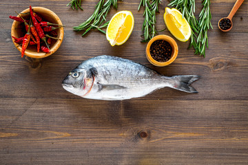 Mediterranian cuisine. Dorado with rosemary, pepper, chili, lemon on wooden background top view copyspace