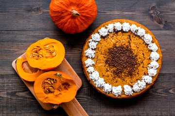 Homemade pumpkin pie decorated whipped cream and chocolate near pumpkins on wooden background top view