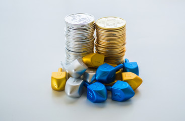 2 stacks of gold and silver Hanukkah coins surrpounded by tiny dreidels isolated on a solid background