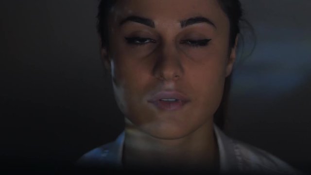 Close-up of a young woman watching a video or film on TV or a computer monitor. Reflection on her face