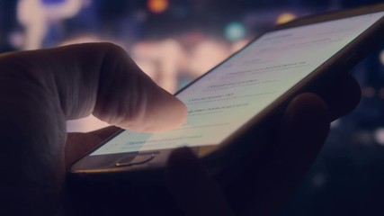 Man is using touching smartphone display outdoors. Blurred city night background
