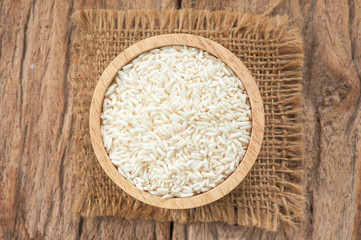 Rice grains in wooden bowl on old wood background