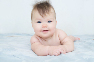 Happy smiling newborn baby portrait cute and adorable in her three month, infant child with blue eyes lying on bed looking at camera