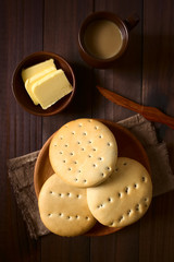 Traditional Chilean Hallulla bread rolls on wooden plate with butter and coffee with milk above,...