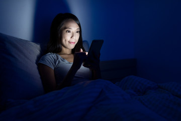Woman working on cellphone and lying on bed at night