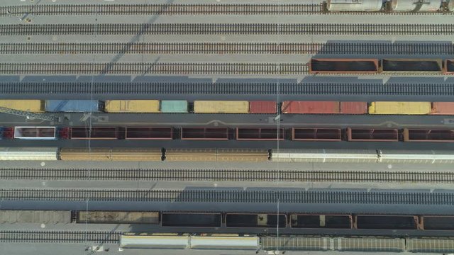 AERIAL TOP DOWN: Flying above empty cargo train moving past freight containers at industrial railroad station on sunny day. Empty railroads and export container trains on industrial railway terminal.