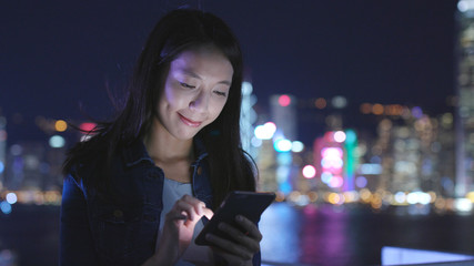 Woman sending sms on cellphone in city at night