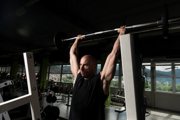 Fototapeta na wymiar Man In The Gym Exercising Shoulder With Barbell