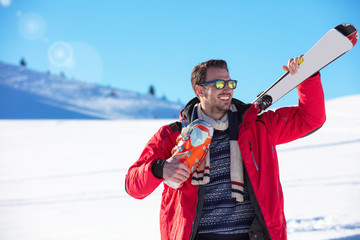 Portrait of healthy man with pair of skis in hands looking aside and smiling