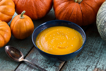 Healthy vegan pumpkin puree in blue bowl decorated with orange and green pumpkins on rustic blue wooden background