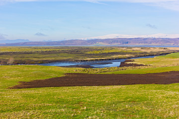 Scenic countryside landscape in Iceland. River flow and volcanic rock formations on horizon.