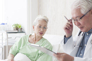 An old doctor is talking to an elderly patient while watching a medical record