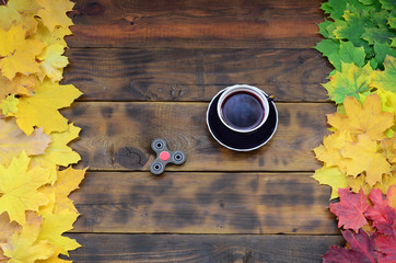 A cup of tea and a wooden spinner among the many yellowing fallen autumn leaves on the background...