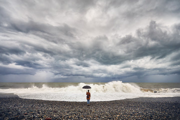 Woman with umbrella near stormy sea