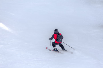 Man skier with red coat and black backpack skiing on fresh white snow on ski slope on Sunny winter day with Copy space in uludag mountain Bursa,Turkey.