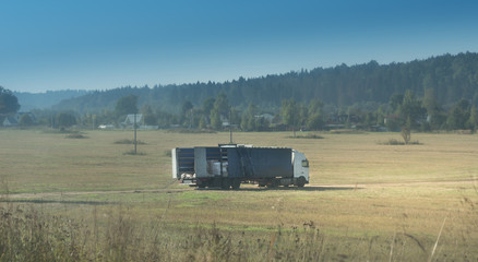 Rural landscape with field road and broken truck, blue sky, green forest