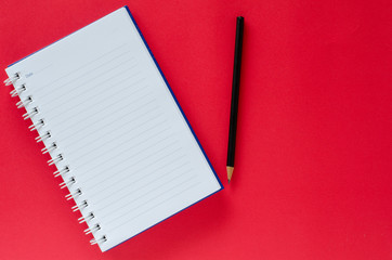 White note book and black pencil on red color background with copy space.