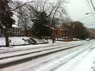 Car tracks down a road in a residential area near a red traffic light after a winter storm