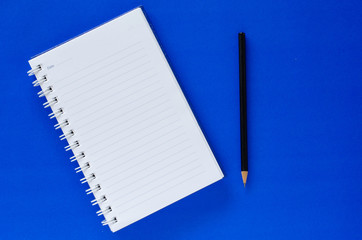 White note book and black pencil on blue color background with copy space.