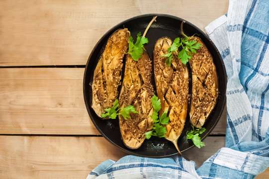 Baked Cut Eggplants In A Black Frying Pan. Eggplants With Honey, Soy Sauce, Pine Nuts. Blue Dish Towel. Place For Text.