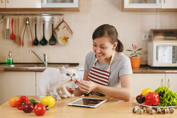 A young pretty woman with white persian cat in the kitchen with tablet on the table. Vegetable salad. Dieting concept. Healthy lifestyle. Cooking at home. Prepare food.