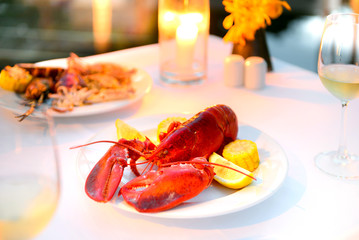 Luxury romantic candle light dinner setup by the pool with plate of lobster and seafood BBQ