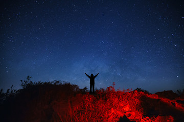 Obraz na płótnie Canvas Landscape with milky way galaxy, Starry night sky with stars and silhouette of a standing sporty man with raised up arms on high mountain.