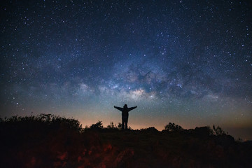 Obraz premium Landscape with milky way galaxy, Starry night sky with stars and silhouette of a standing sporty man with raised up arms on high mountain.