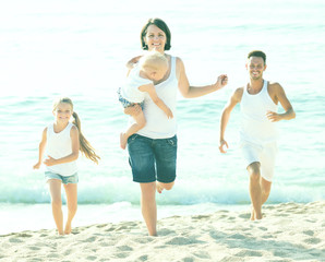 family of four running on sandy beach on sunny weather