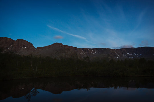 The sky with the stars at dawn, reflected in the water of a mountain lake.