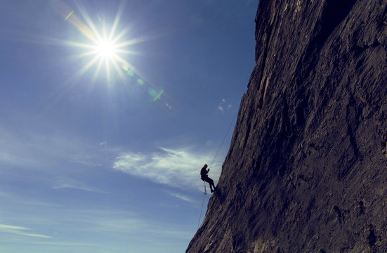 The climber makes a descent on a rope on the wall against the background of the sun.