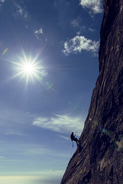 The climber makes a descent on a rope on the wall against the background of the sun.
