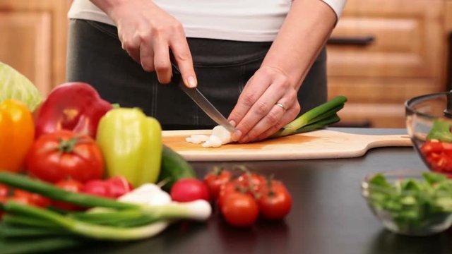 Woman hands chopping spring onion for a vegetables salad - side view  of the cutting board at the kitchen table, camera slide