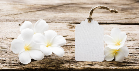 Fototapeta na wymiar White paper tag label decorate with plumeria flowers on rustic wood table