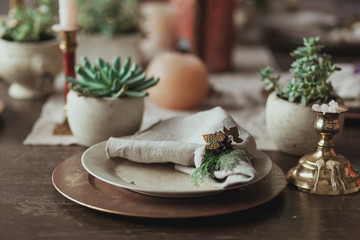 Rustic wooden table serving with succulents in concrete pot, candles, sackcloth napkin. Plates in focus