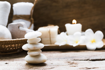 White zen stones and spa and treatment settting with towels,scrub,coconut soap and frangipani flowers on rustic wooden background