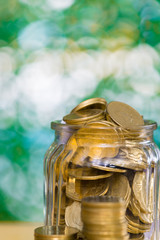 Gold coin money in the glass jar on table in garden with green background, for saving banking financial concept.