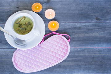 Good sleep concept, sleeping mask and a cup of herbal tea on the wooden table.