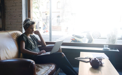 Blonde hipster girl is reading emails on a screen of a modern portable computer while sitting in a...