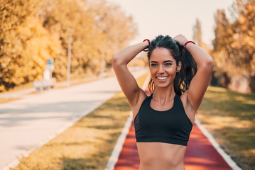 Fit female athlete tying hair before her workout outdoors on running track.