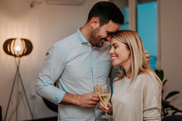 Lovely couple drinking wine while hugging in their living room.