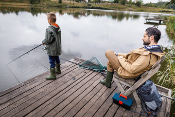 Father and son fishing with rods on wooden pier at lake