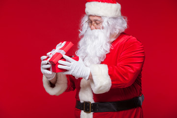 Christmas. Photo Santa Claus giving xmas present and looking at camera, on a red background