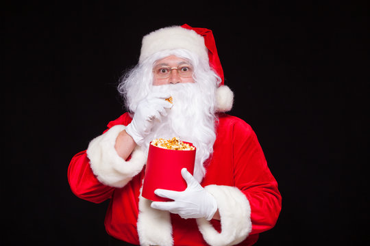 Christmas. Photo of Santa Claus gloved hand With a red bucket with popcorn, on a black background